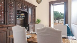 A dining area with a wooden table, white chairs, and a television on a cabinet.