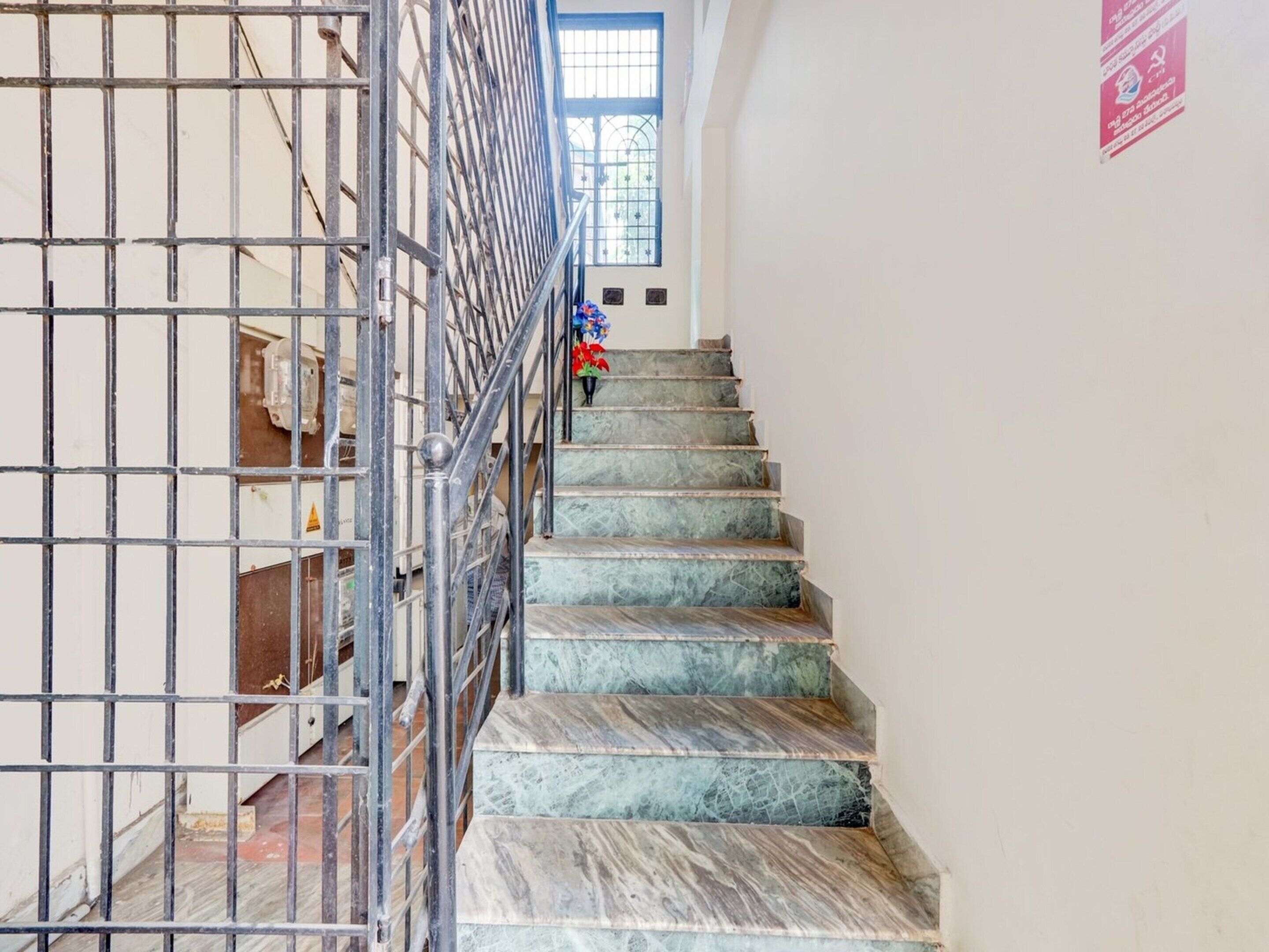 Un escalier avec des rampes en métal, une fenêtre bleue et une enseigne rouge sur le mur.