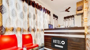 A hotel reception area with a wooden reception desk, two red chairs, a ceiling fan, and patterned curtains. - Super Hotel O Adarsh Nagar (Visakhapatnam)
