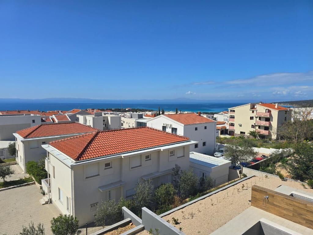 A residential area with white buildings, red-tiled roofs, and a clear view of the sea.