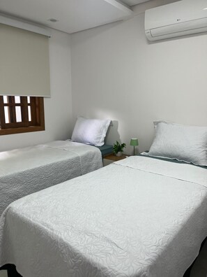 Une chambre avec deux lits, une fenêtre avec des stores, une table de chevet avec une lampe et un appareil de climatisation.