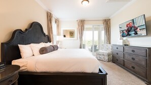 A bedroom with a large bed, a dresser, a chair, and a TV on the wall. - 6BR Home w/ Pool, Theater & Game Room (Kissimmee)