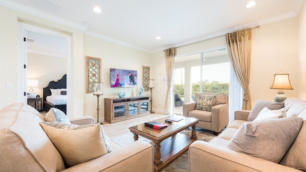 A spacious living room with a large sofa, a coffee table, and a television mounted on the wall. - 6BR Home w/ Pool, Theater & Game Room (Kissimmee)