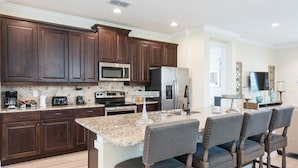 A kitchen with dark wood cabinets, a granite countertop, a built-in microwave, a stainless steel refrigerator, a gas stove, and a bar area with bar stools. - 6BR Home w/ Pool, Theater & Game Room (Kissimmee)