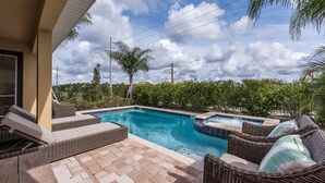 A swimming pool with lounge chairs and a hot tub, surrounded by greenery. - 6BR Home w/ Pool, Theater & Game Room (Kissimmee)