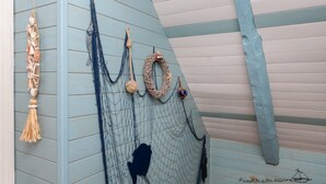 Un muro decorato a tema nautico, con un pannello macramè fatto con corda, una rete con la sagoma di un pesce e una corda con un oggetto blu.