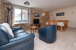 Ein Wohnzimmer mit einer Steinwand, einem Ledersofa, einem Fernseher und einem Essbereich mit Holztischen und -stühlen.