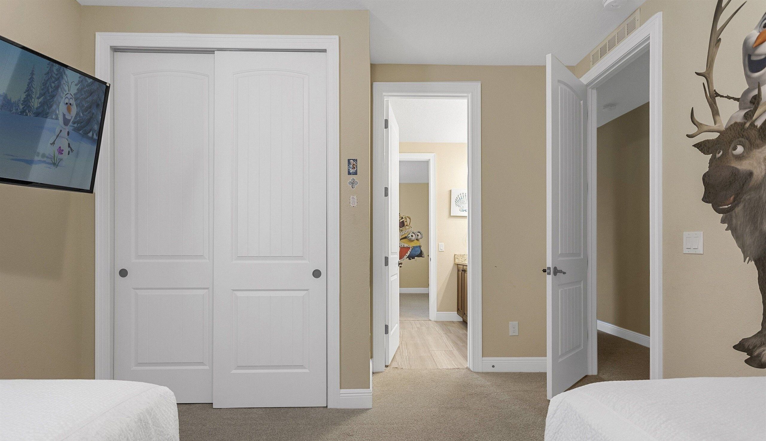 Un dormitorio con dos camas, una puerta blanca y un pasillo que conduce a otra habitación.