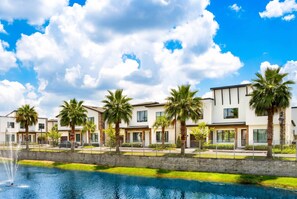 A modern hotel with a pool, palm trees, and a clear blue sky. - 5BR Family Home w/ Private Pool  / Near Disney (Davenport)