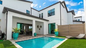 Ein modernes, zweistöckiges Haus mit Pool, Terrassenbereich und umzäunter Garten.