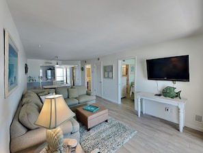 A living room with a sofa, a coffee table, a TV, and a dining area in the background. - Pointe South 302 | Gulfside Escape + Resort Pool (Fort Myers Beach)