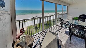 A balcony with a view of the beach, wicker furniture, and a ceiling fan. - Pointe South 302 | Gulfside Escape + Resort Pool (Fort Myers Beach)