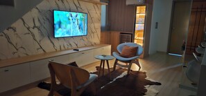 A modern living room with a flat-screen TV, wooden furniture, a glass cabinet, and a fur rug.