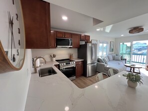 A modern kitchen with a large island, stainless steel appliances, and a view to a balcony. - Charming 2-Bedroom with Water View & Boat Slip in Carolina Beach (Carolina Beach)