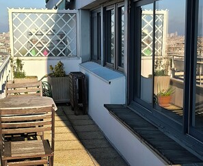 Eine Dachterrasse mit einer Holzbank, Blumentöpfen und Blick auf die Stadtlandschaft.