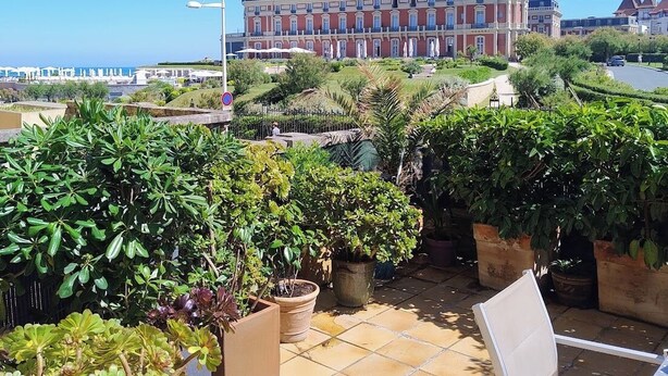 Ein Hotel mit einem großen Gebäude, einer Terrasse mit Blumentöpfen und einem Stuhl.