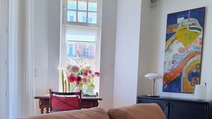 Ein Wohnzimmer mit einer Couch, Kissen, einem Tisch mit Blumen und einem Bild an der Wand.