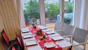Ein Essbereich mit einem Tisch für sechs Personen, großen Fenstern und Blick auf Gebäude und Grünflächen.