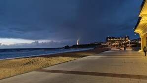 Eine Küstenpromenade mit Strand, Leuchtturm und einem Gebäude mit beleuchteten Fenstern.