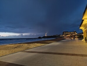 A coastal promenade with a beach, a lighthouse, and a building with illuminated windows. - For rent : Beautiful bright apartment - ideally located (Biarritz)