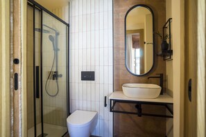 Un baño con ducha envuelta en vidrio, un inodoro blanco y un lavamanos con un espejo arriba.