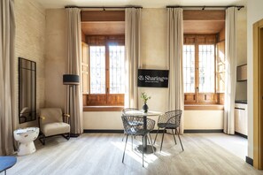 Une chambre d’hôtel dotée d’une grande fenêtre, d’un téléviseur à écran plat fixé au mur, d’une table ronde avec deux chaises, d’un lampadaire et d’un canapé.