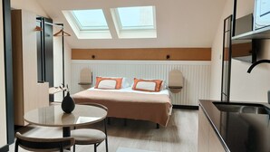 A compact hotel room with a bed, a small round table, a chair, a desk, a kitchenette, and a skylight. - Housing Fana by Sharing Co 3PAX (Málaga)