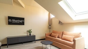 A modern living room with a sofa, a small round table, a potted plant, a black console, and a sign on the wall. - Housing Fana by Sharing Co 3PAX (Málaga)