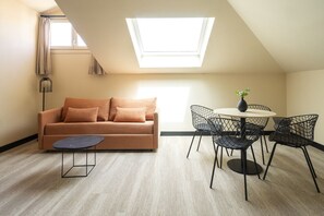 A modern loft bedroom with a sloped ceiling, a sofa, a small table, a round dining table with chairs, and a skylight. - Housing Fana by Sharing Co 3PAX (Málaga)