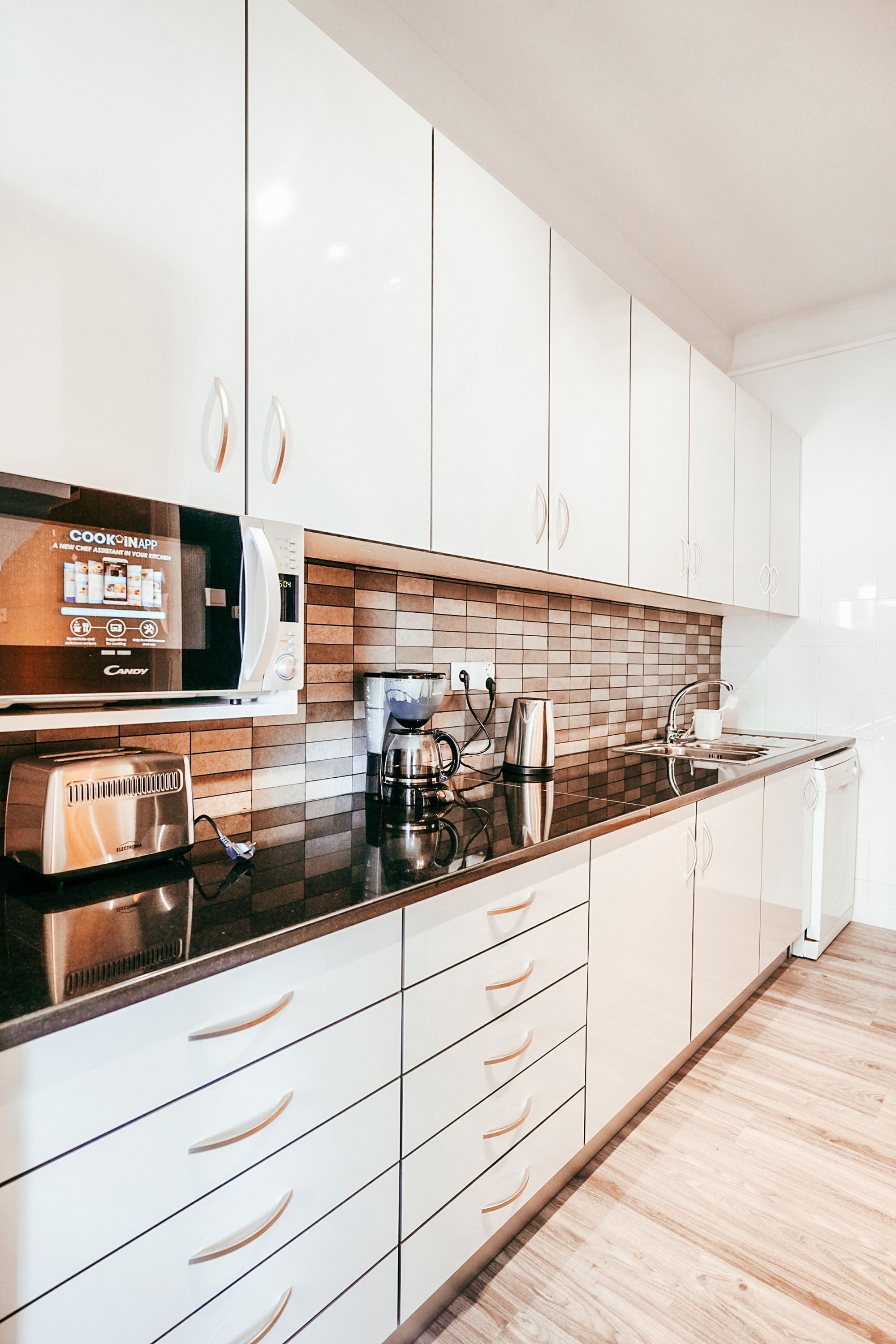A modern kitchen with white cabinets, a microwave, a toaster, a coffee maker, and a sink.