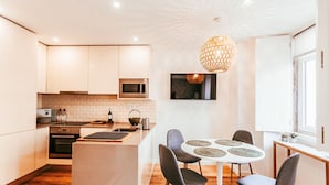 A modern kitchen with white cabinets, a microwave, and a dining area with a round table and chairs. - Prestige Apartment By Gt House (Lisbon)