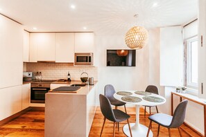 A modern kitchen with white cabinets, a microwave, and a dining area with a round table and chairs. - Prestige Apartment By Gt House (Lisbon)