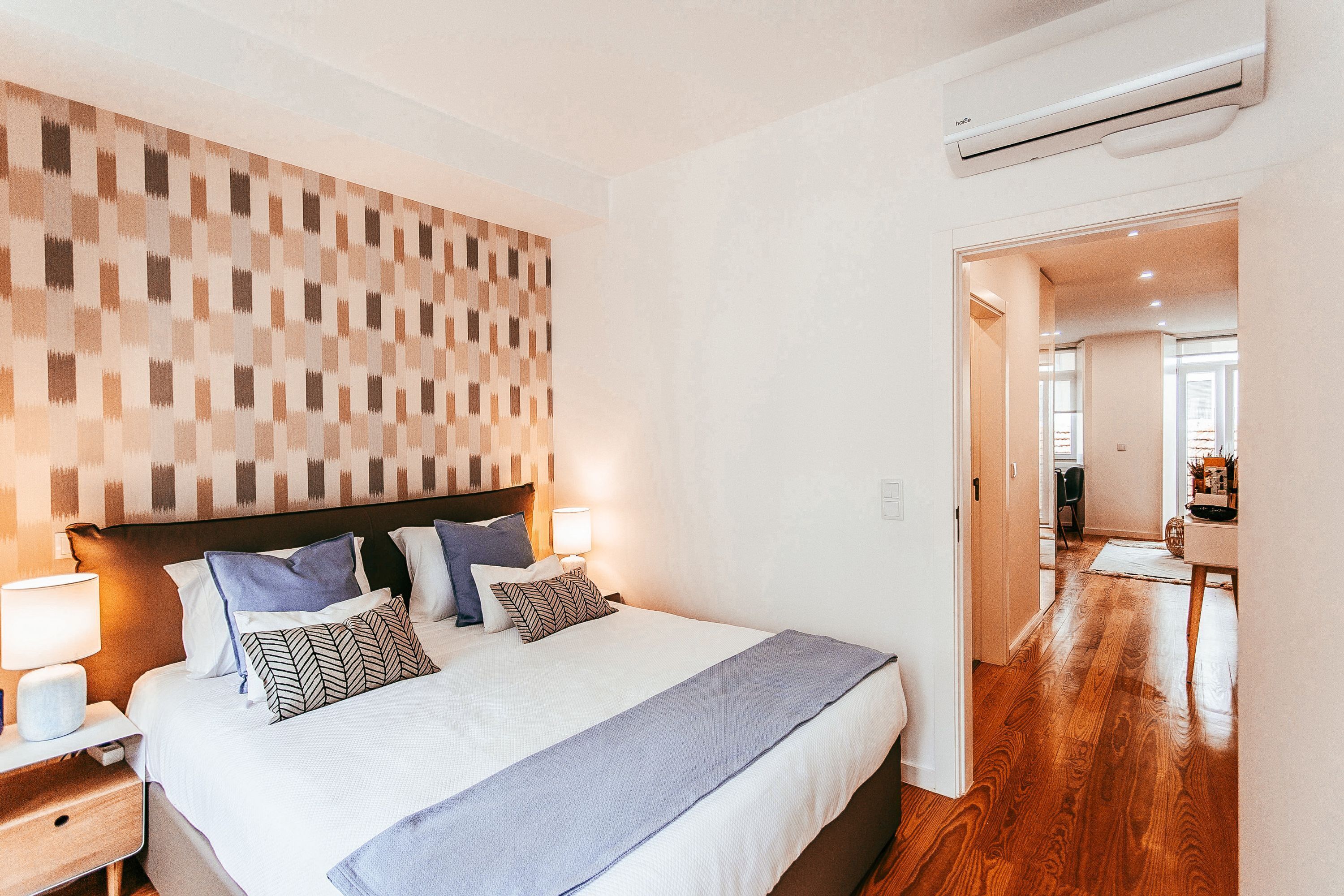 Un dormitorio con una cama grande, lámparas de noche, un aire acondicionado instalado en la pared y un pasillo que conduce a un comedor.