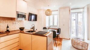 A modern kitchen with a microwave, sink, and dining area with chairs and a table. - Prestige Apartment By Gt House (Lisbon)