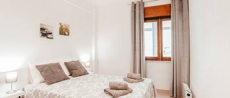 Un dormitorio con una cama, dos lámparas de pared, un ventanal con cortinas y un dispositivo montado en la pared.