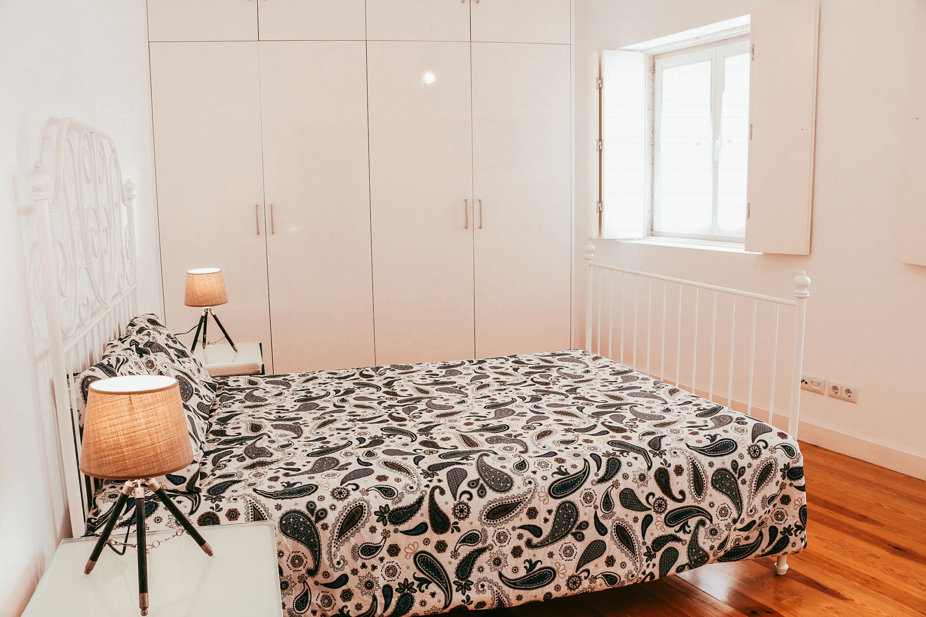 A bedroom with a bed, a bedside lamp, a wardrobe, and a window.