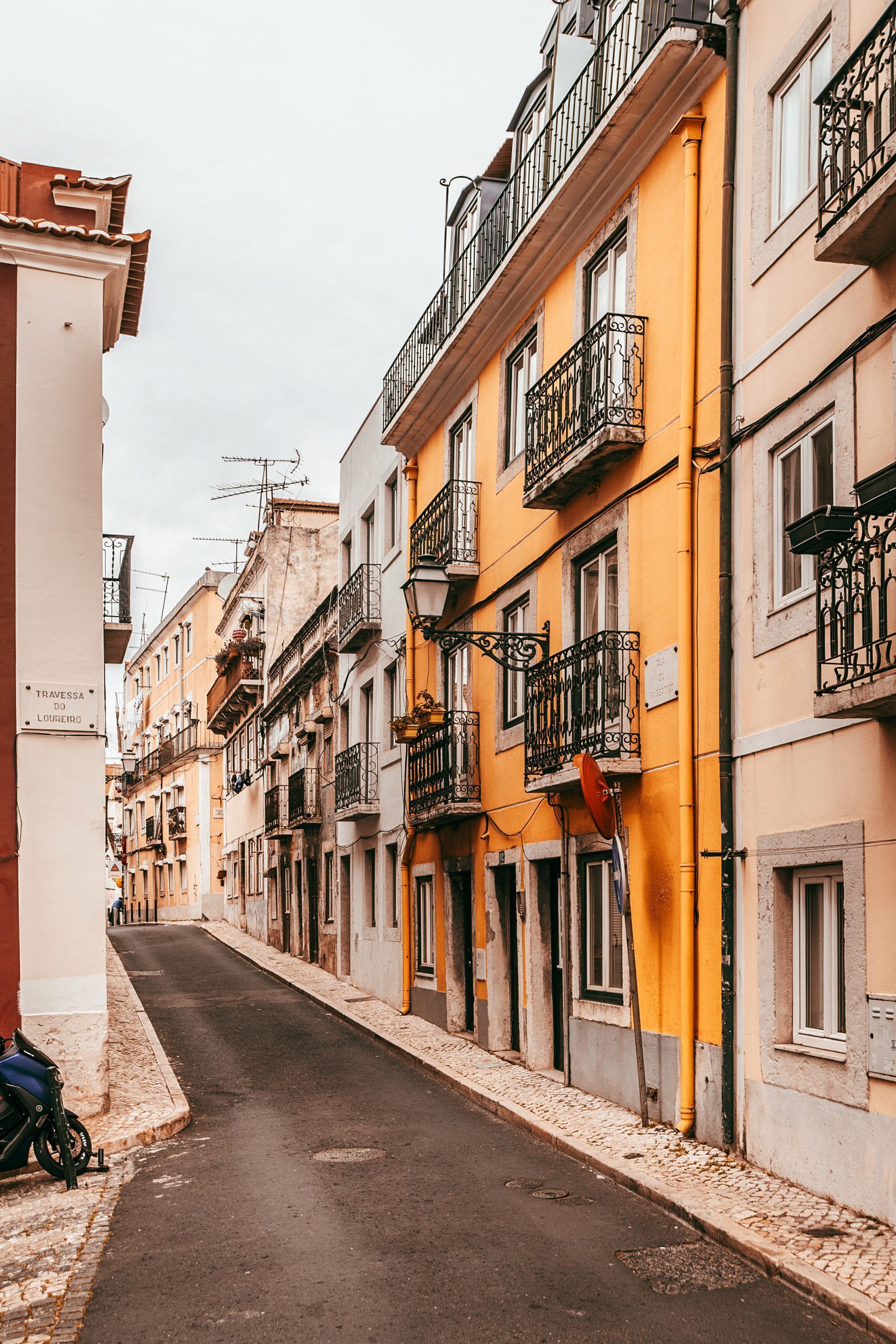 Une rue étroite bordée d’immeubles à plusieurs étages, dont certains sont dotés de balcons et d’une enseigne indiquant un lieu.
