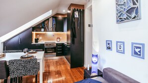 A modern kitchen with dark cabinetry, a dining area with patterned chairs, and a living space with a sofa and wall art. - Central Typical Lisboa by GT House (Lisbon)