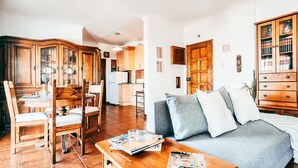 A living room with a sofa, a wooden dining table with chairs, a kitchen area, and a wooden cabinet with glass doors. - Amadora Terrace View By Gt House (Amadora)