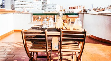Mesa de madera con sillas en una terraza en la azotea, con vista a la ciudad.