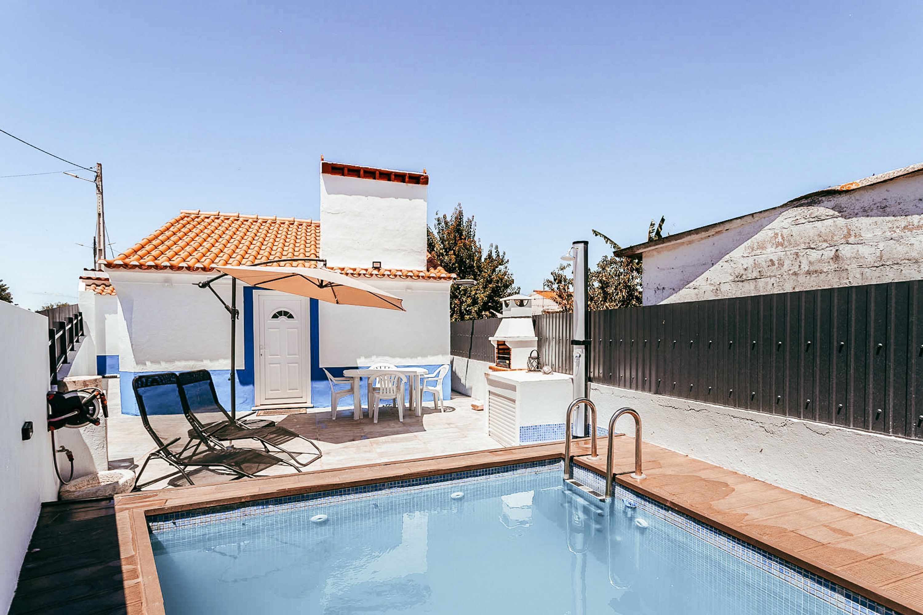 A swimming pool with lounge chairs, a table, and a barbecue area.