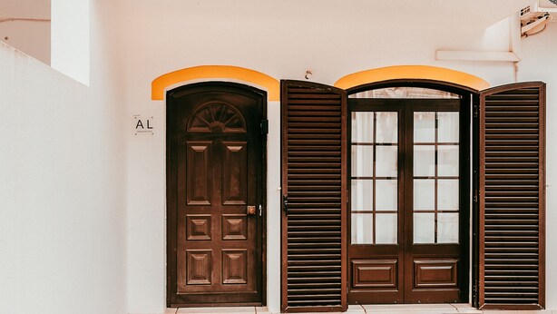A set of three doors with a brown finish, each with a different style of window and door design, set against a white wall with a tiled floor. - Altura Beach Villa by GT House (Castro Marim)