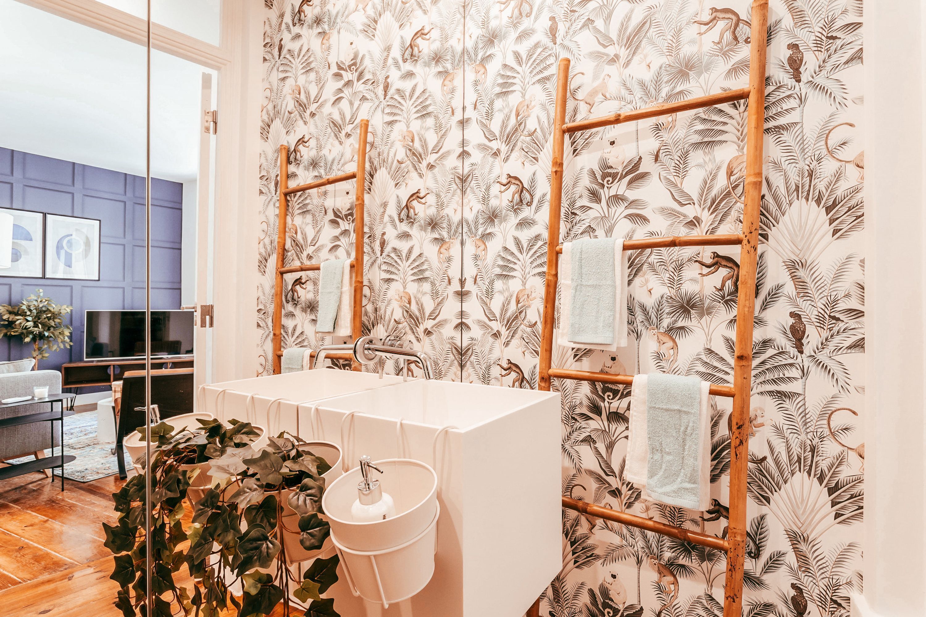 A bathroom with a white sink, a mirror, and a towel rack against a wall with a leaf pattern.