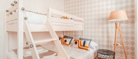 Una cama litera con escalera, una lámpara de noche y un cubo de basura pequeño.