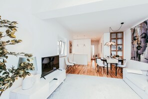 A modern living room with a flat-screen TV, white furniture, a dining area with a wooden table, and a large abstract painting. - Modern Charming Alges by GT House (Oeiras)