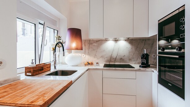 Una cocina moderna con armarios blancos, encimera de madera, horno empotrado y una lámpara colgante.