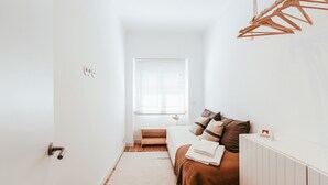 Un dormitorio con cama, mesita de noche, radiador, ventana con persianas y perchero.