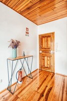 Teto de madeira, porta de madeira, uma pequena mesa com um vaso e um extintor de incêndio.