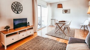 Una sala de estar moderna con un televisor de pantalla plana, mueble de madera para entretenimiento y un comedor con mesa y sillas.