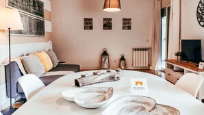 Una sala de estar moderna con un sofá blanco, una mesa de comedor con platos decorativos, un televisor y un cartel que indica 'GT HOUSE'.